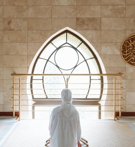 femme portant le hijab de dos devant une fenêtre remplie de lumière annour