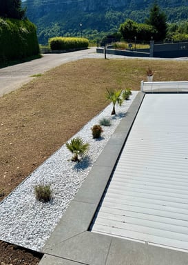  Aménagement paysager autour d'une piscine avec graviers blancs et palmiers.
