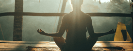Person meditating in lotus position during sunrise at a tropical wellness retreat
