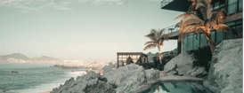 Modern cliffside villa with ocean view, palm trees, and infinity pool at sunset