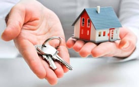 Manos sosteniendo una maqueta de casa junto a una llave, representando seguridad en la gestión