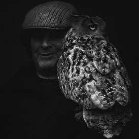 A man, in shadow, holds an owl on his arm on The High Street, Edinburgh
