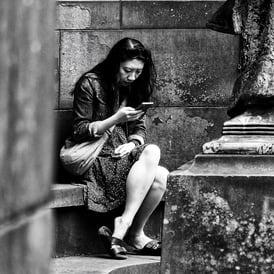 A woman sits scrolling on her phone in Princes Street Gardens
