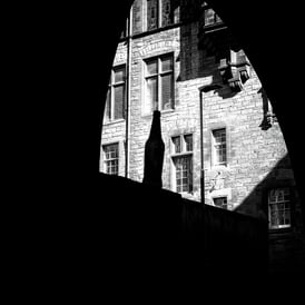 An empty bottle, perched on a wall, silhouetted against a bright building in The Cowgate, Edinburgh