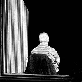 A man, lit by the sun on his back, sits in a cafe window, in shadow on St Mary's Street, Edinburgh