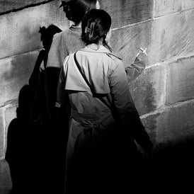 Two women walk, half covered in shadow, along East Market Street, Edinburgh