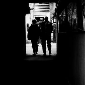 A couple emerge from a shadowy close into a courtyard. The High Street, Edinburgh