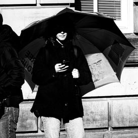 A woman stands looking at her phone, her face half covered in the shadow from her umbrella on The High Street, Edinburgh