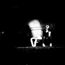A woman, in sunlight, sits on a bench, eating, in an almost total shadow background at Lochrin Basin, Edinburgh