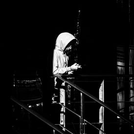 A man in a hoodie stands in a doorway half lit by the sun against a black background at Lochrin Basin, Edinburgh