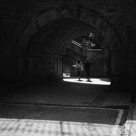 A couple walk under a bridge into a pool of light at Saunders Street, Edinburgh