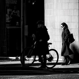 A woman on her bike, in shadow, and a woman behind her in the light at the bottom of Morningside Road, Edinburgh