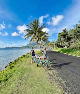 Eva et Manon en vélo devant des palmiers et le lagon bleu de Bora