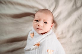 Newborn wrapped in a white swaddle with gold hearts, looking directly at the camera during a Hibbing