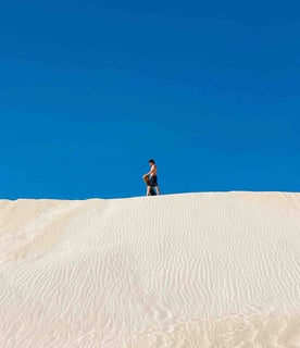 Man at the top of the sand dunes with his snowboard in Lancelin, Western Australia.