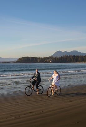 bride and groom riding bicycles on a beach