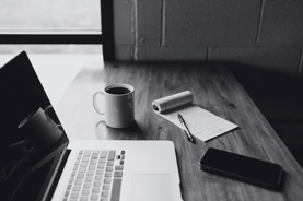 A work desk with laptop, coffee mug, notepad, pen and phone | translation services