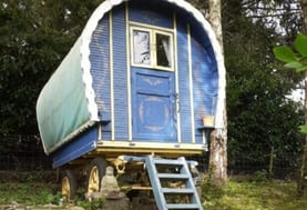 Colorful bow-top gypsy wagon with blue and yellow paint, garden roulotte with ladder entrance, Buddh