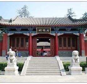 a chinese temple with a large red building and a few statues