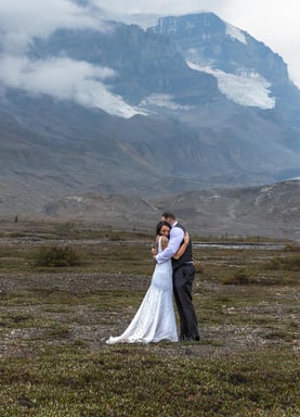 a bride and groom standing at the athabasca icefeilds