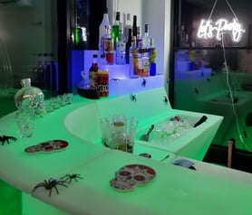 SweetAz Co. corner LED glow bar setup featuring Halloween-themed liquor, syringes, and ice, with a โLetโs Partyโ neon sign gl