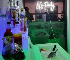 Green glow bar with blue glow drink stand with lets party neon in the background in Redlands.