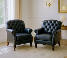 Two tufted black leather armchairs in a bright living room with soft drapes, sconces, and mirror.