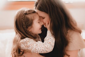 Mother and daughter share a tender moment with foreheads touching and eyes closed, as the little gir