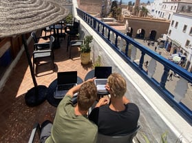 two men sitting at a table with laptops