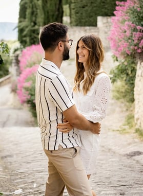 Smiling couple in a Provençal village alley with pink flowers — fine art editorial session