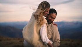 Un homme portant sa femme à la montagne tout deux habillé de blanc et de beige.