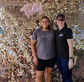 Carly and Linelle, standing in front of a rose gold shimmer wall with a ‘Forty’ neon sign, for her birthday in Brisbane.