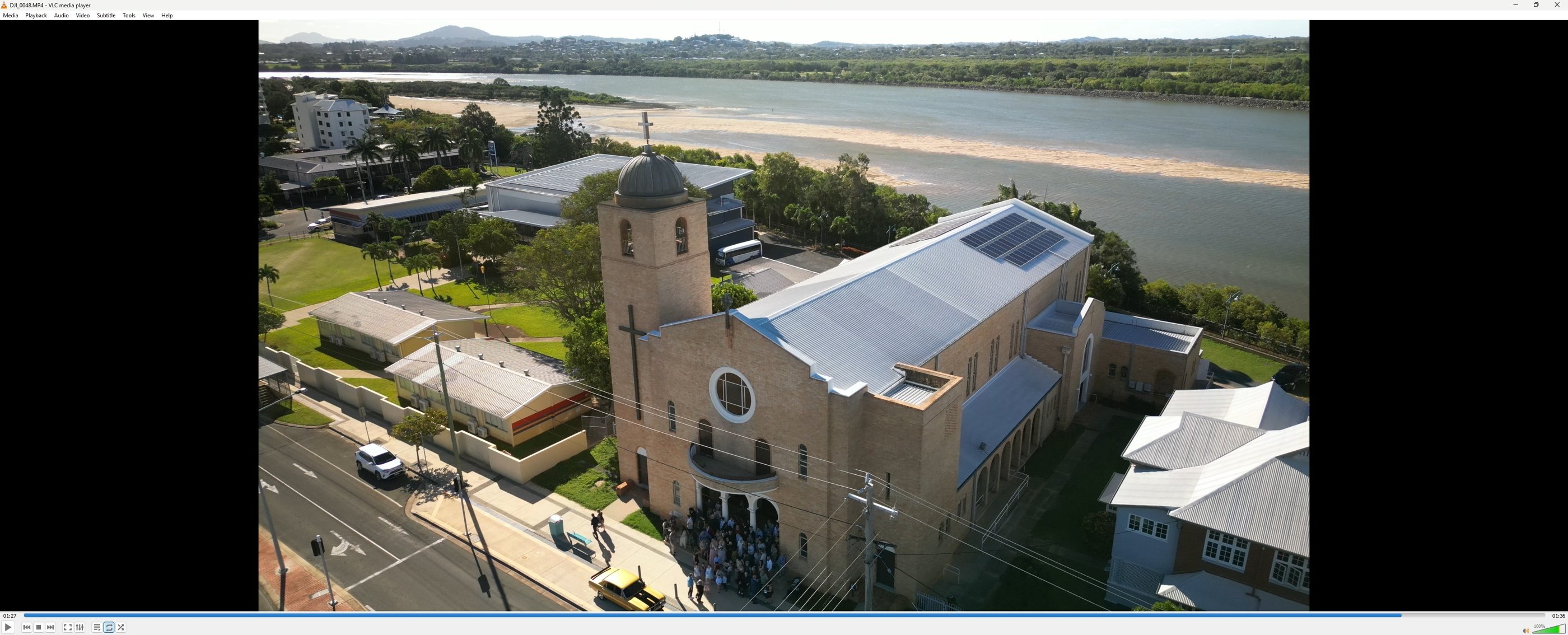 Aerial view of a brick church with solar panels on the roof near a river in a coastal town.