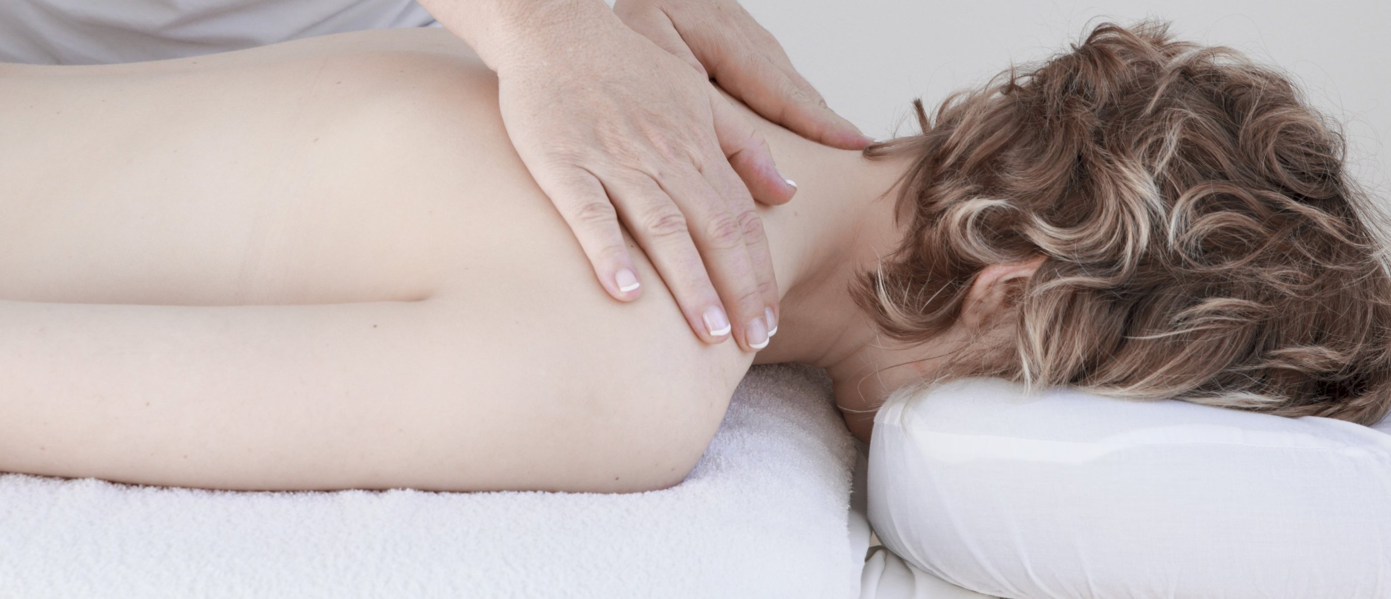 Professional massage therapist performing a therapeutic neck and shoulder massage on a relaxed female client.