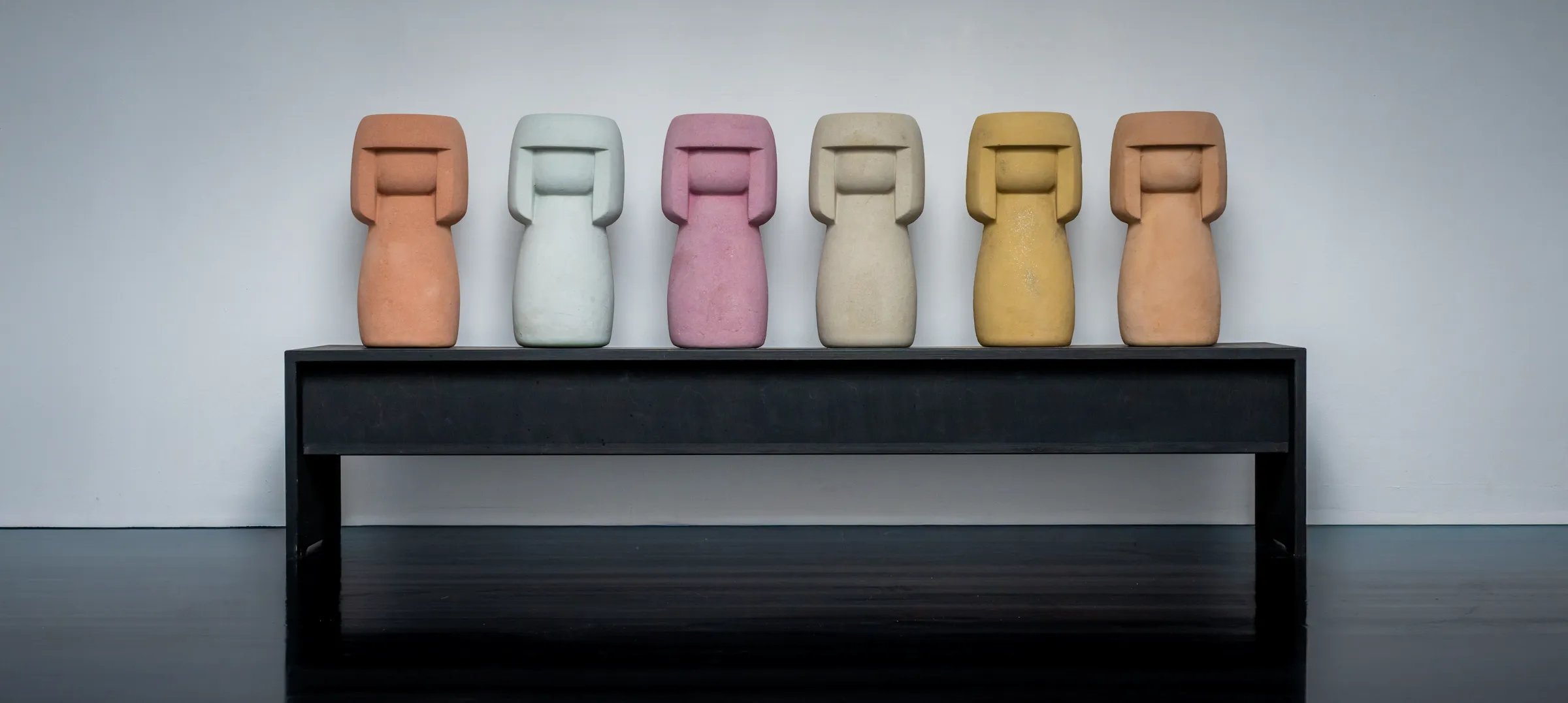 Sechs Kokeshis stehen nebeneinander auf einer Bank.