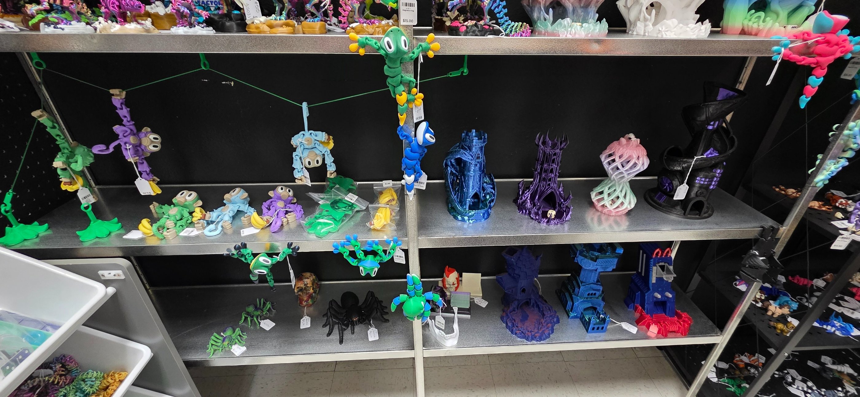 A retail shelf display featuring colorful 3D printed toys, articulated monkeys, and fantasy dice towers.