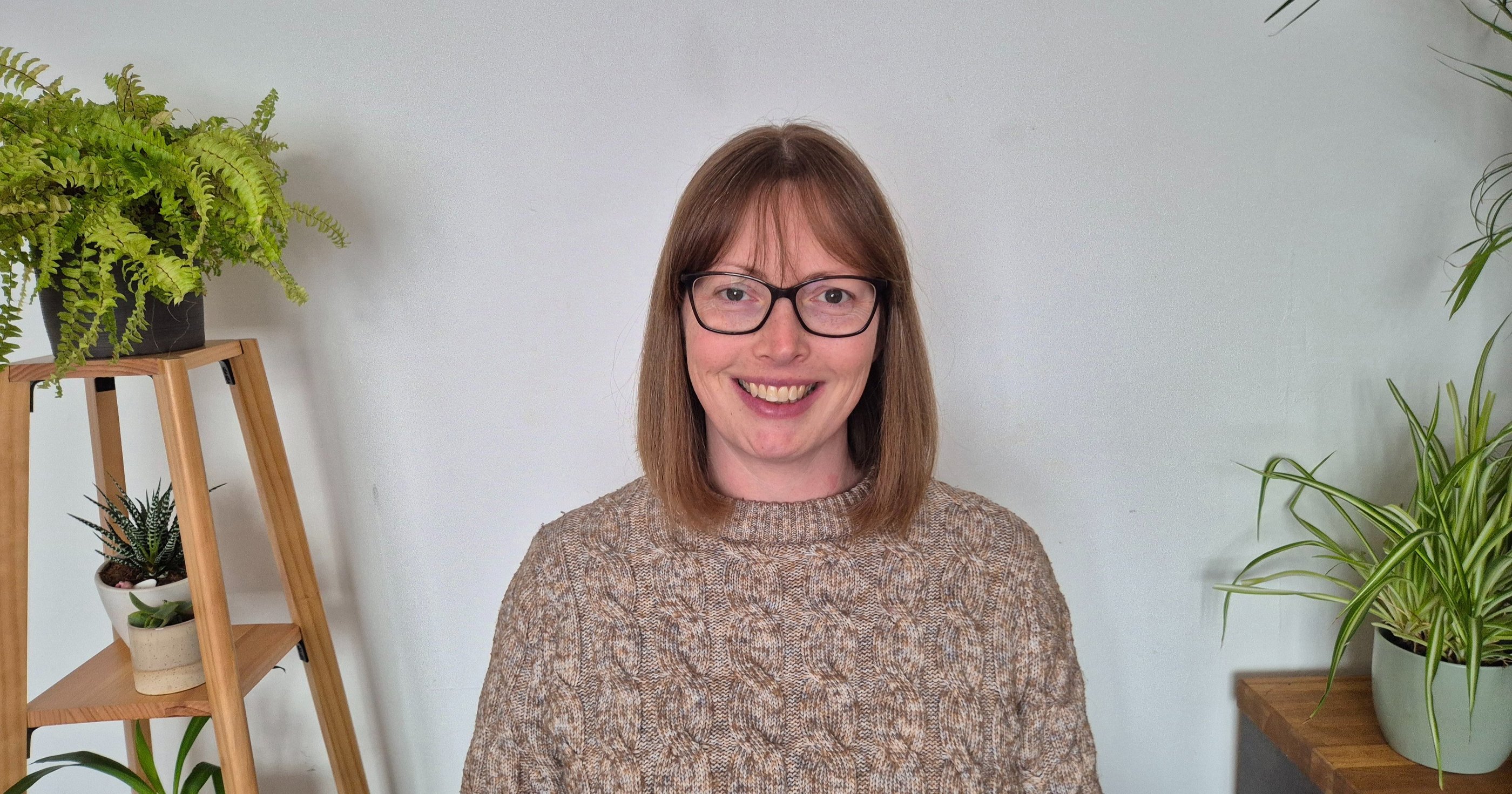 A smiling woman sits between leafy green plants
