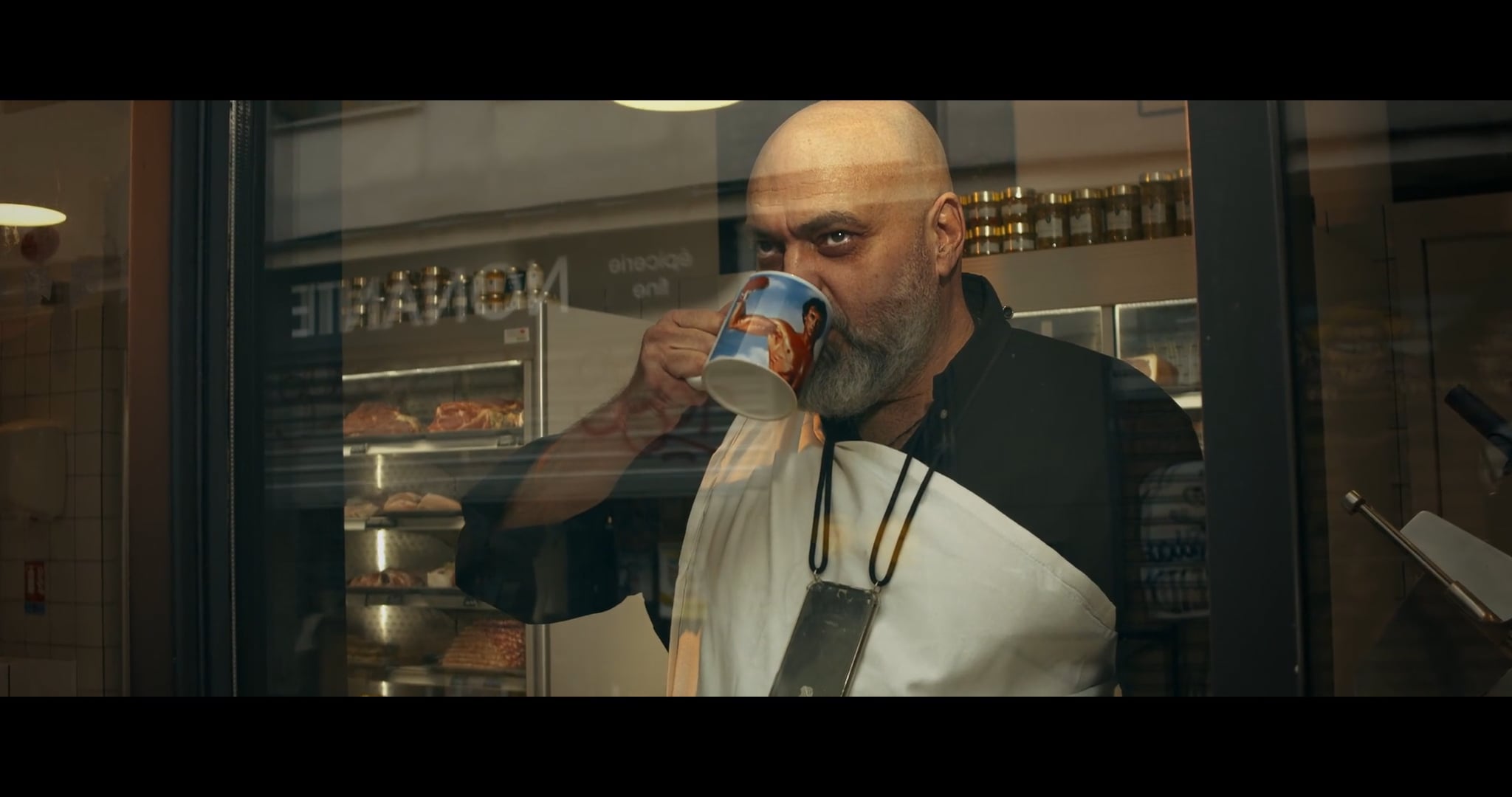 un homme en tenue de boucher tient un mug sur lequel on peut voir Sylvester Stallone en Rocky