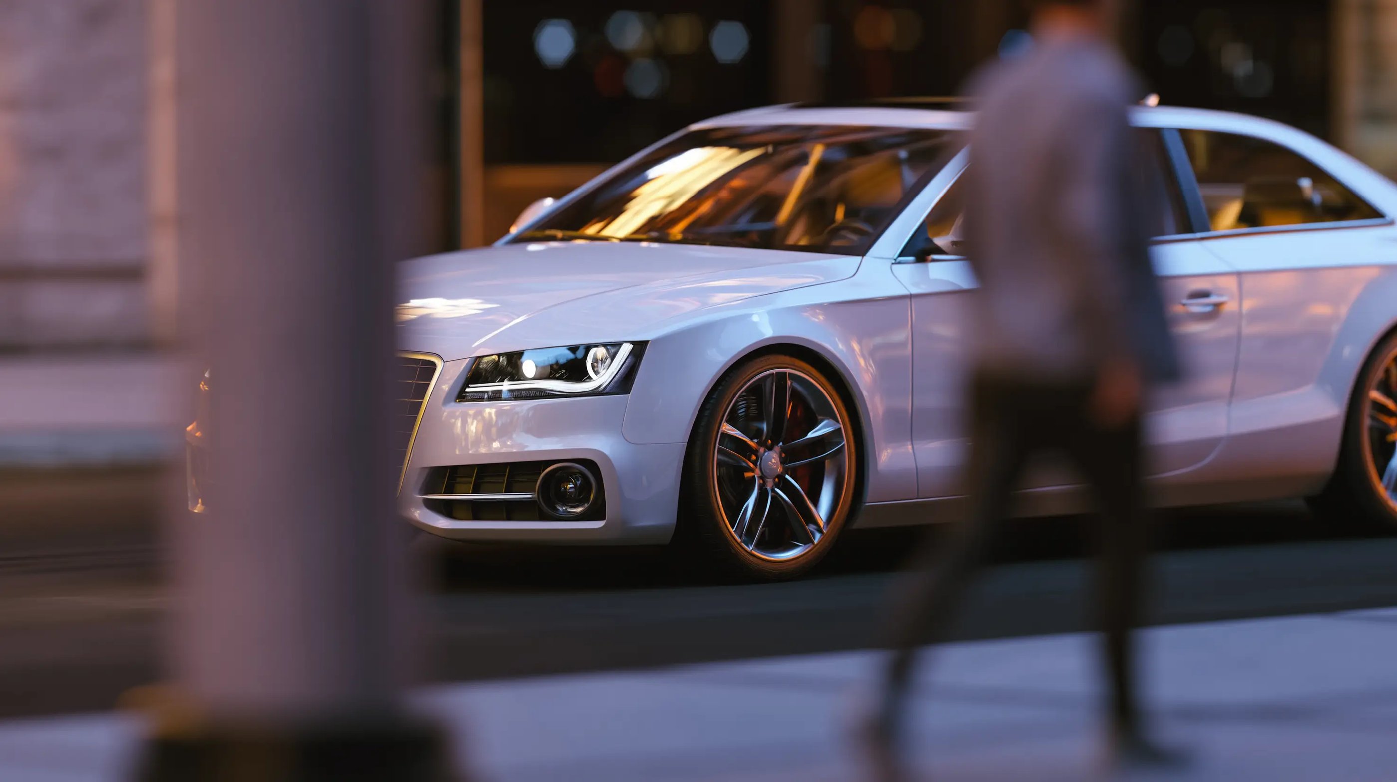 A white luxury sedan parked on a city street at night with glowing headlights and blurred city lights.