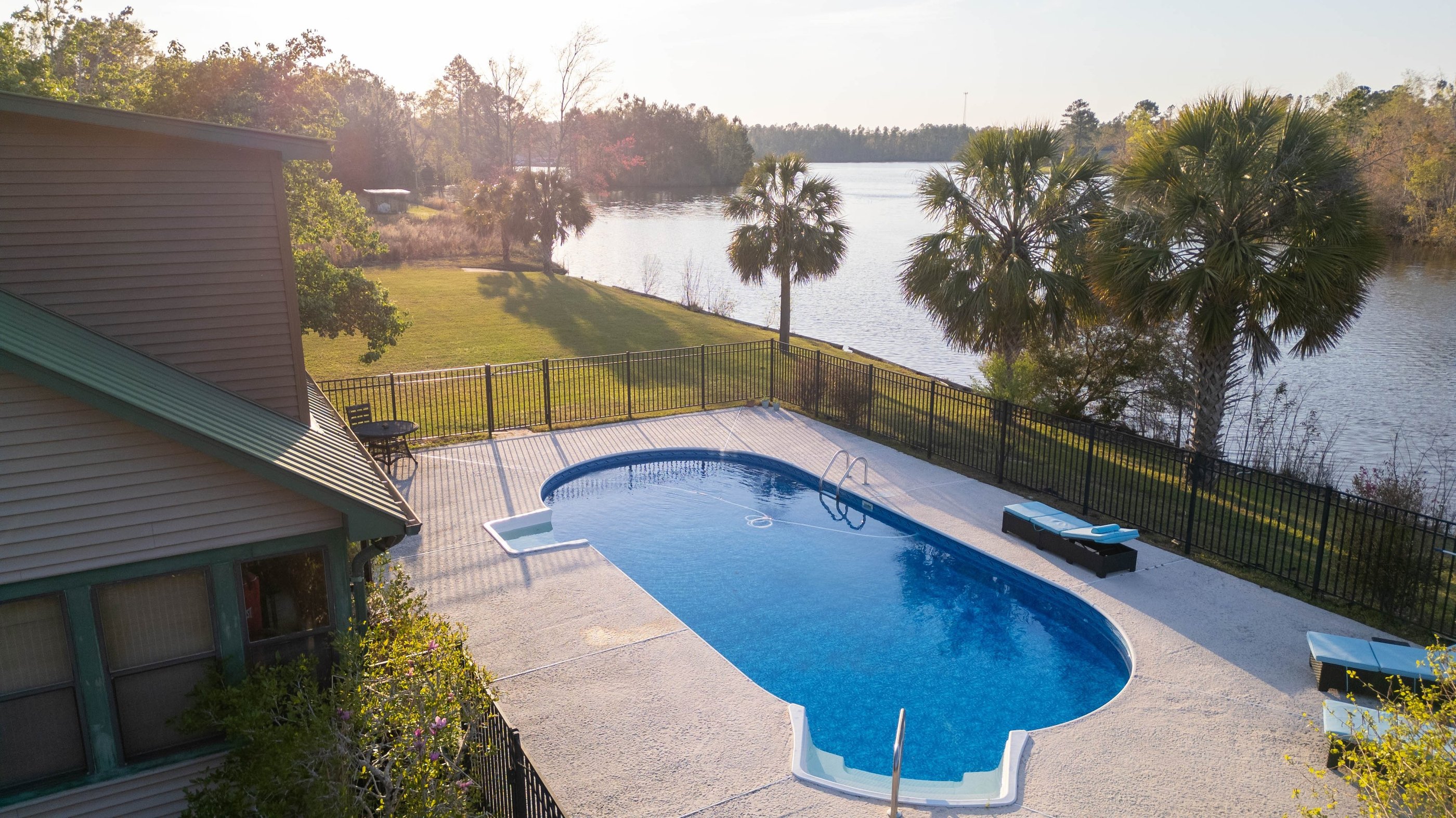 a pool with a fenced in area with a bench and chairs