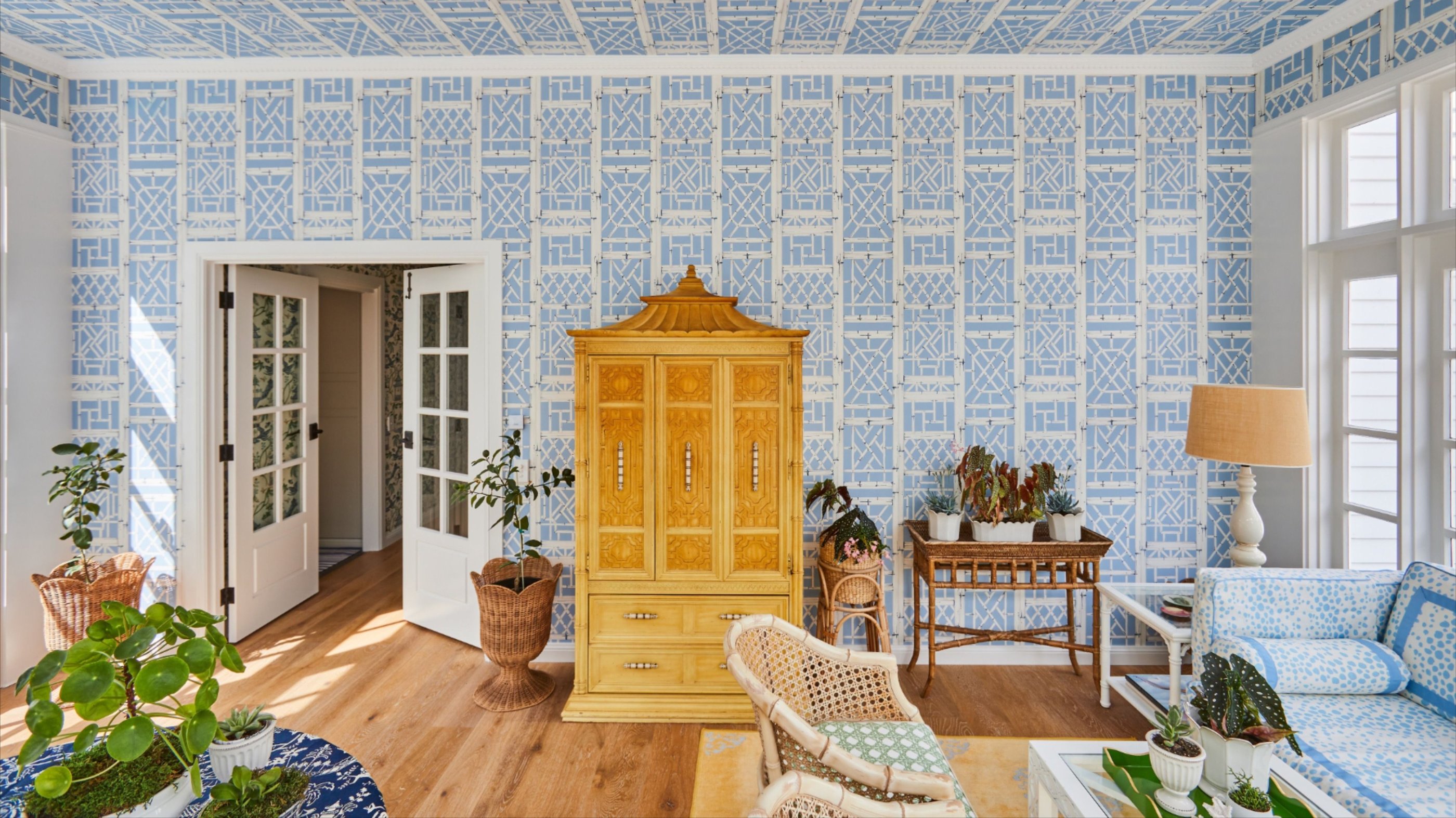 Elegant sunroom featuring blue geometric lattice wallpaper, an ornate yellow Chinoiserie armoire, and lush indoor plants.