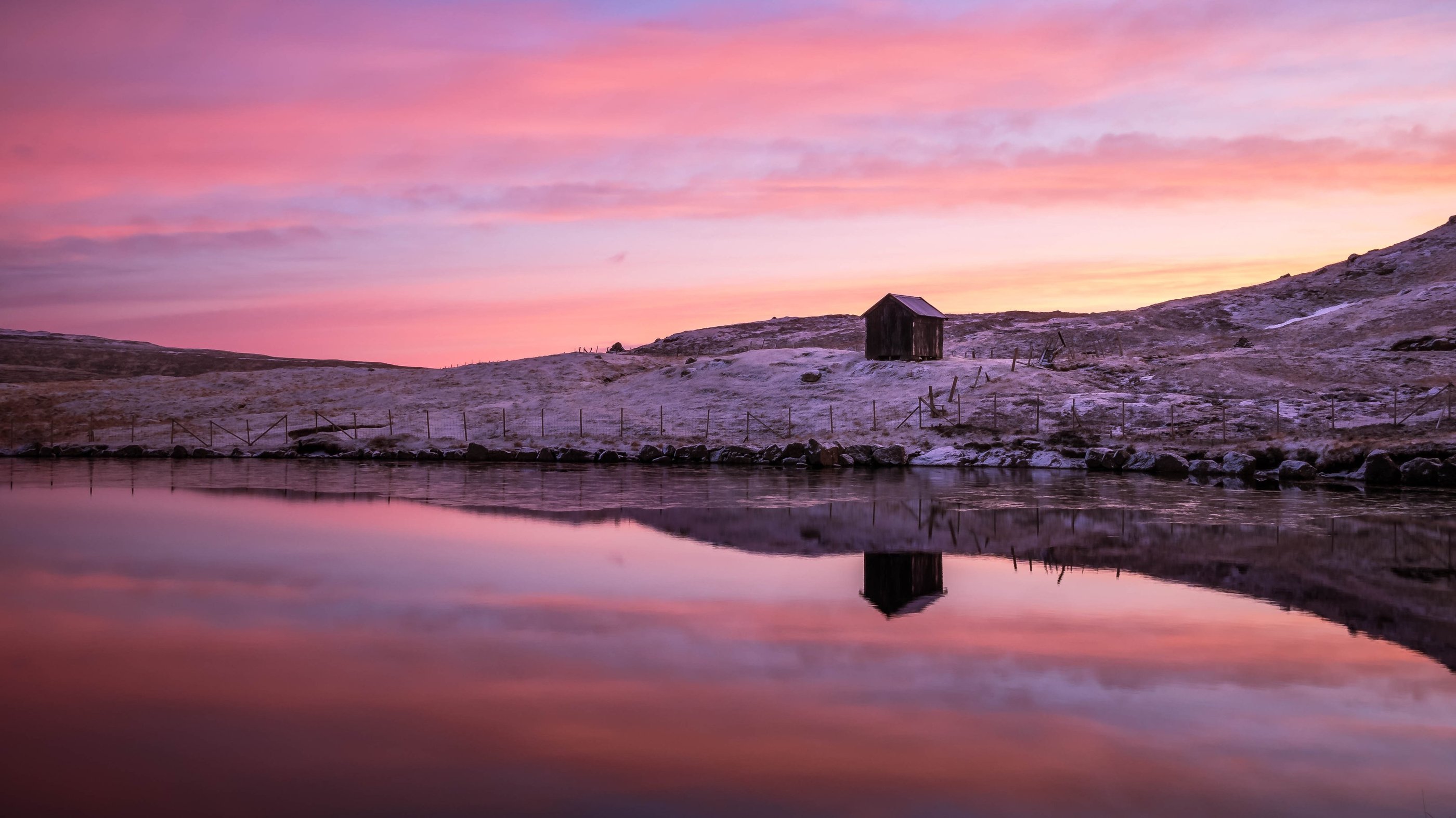 Lake near Nes on Eysturoy reflecting sunset sky and surrounding hills, calm and minimalist Faroe Islands landscape