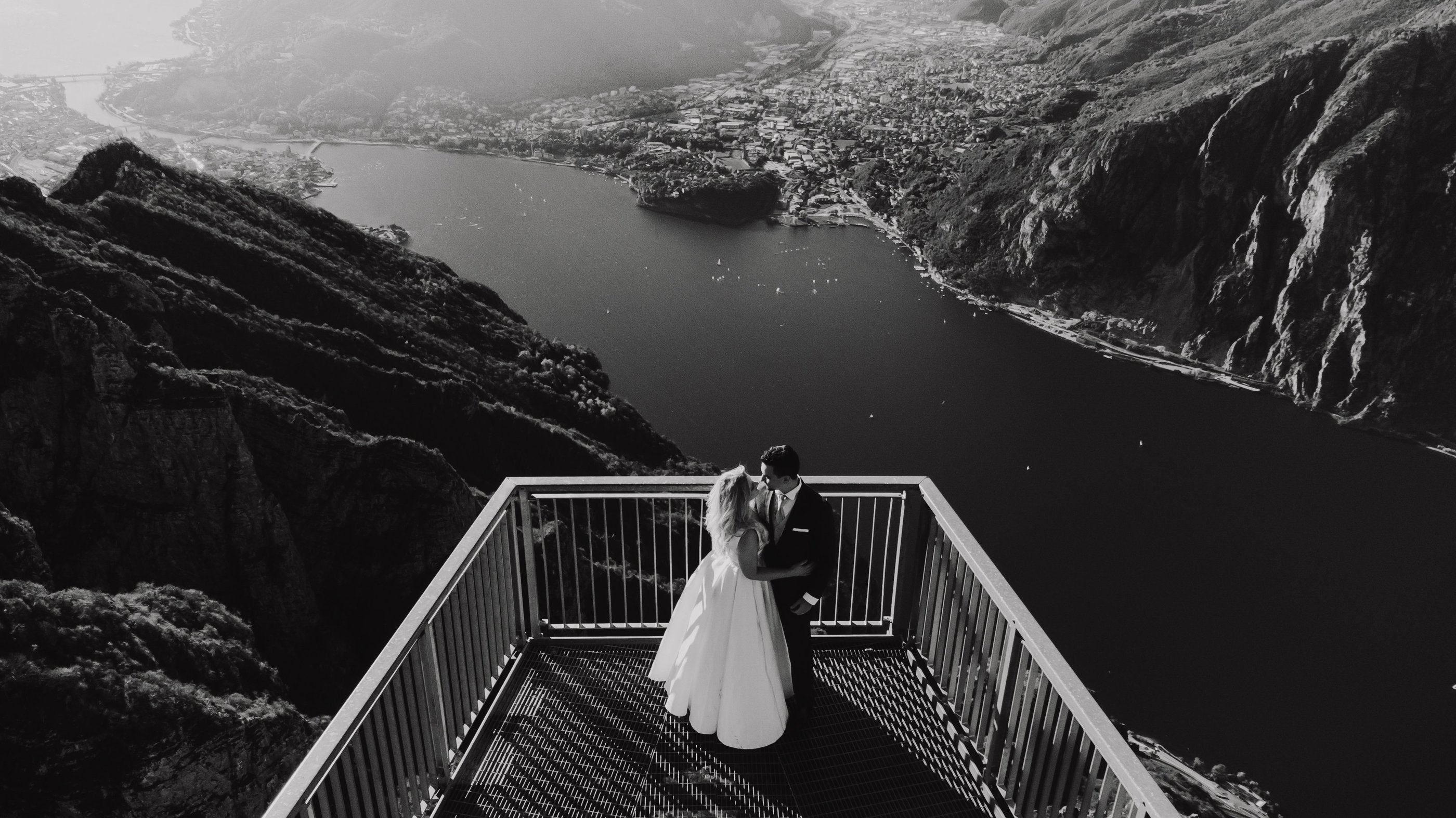 a bride and groom standing on a balcony railing overlooking a mountain