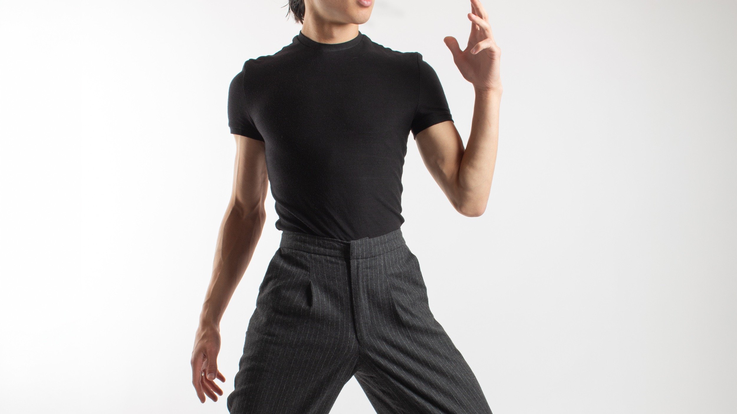 A man wearing a black slim-fit t-shirt and charcoal pinstripe trousers against a white background.