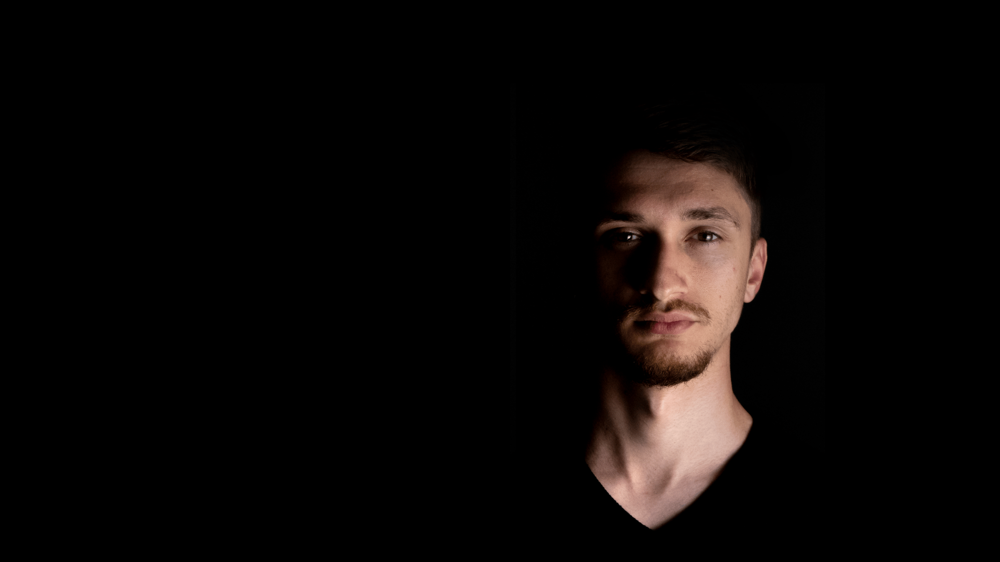 Close-up shot of music artist Valah's face in the dark, illuminated by dramatic lighting.