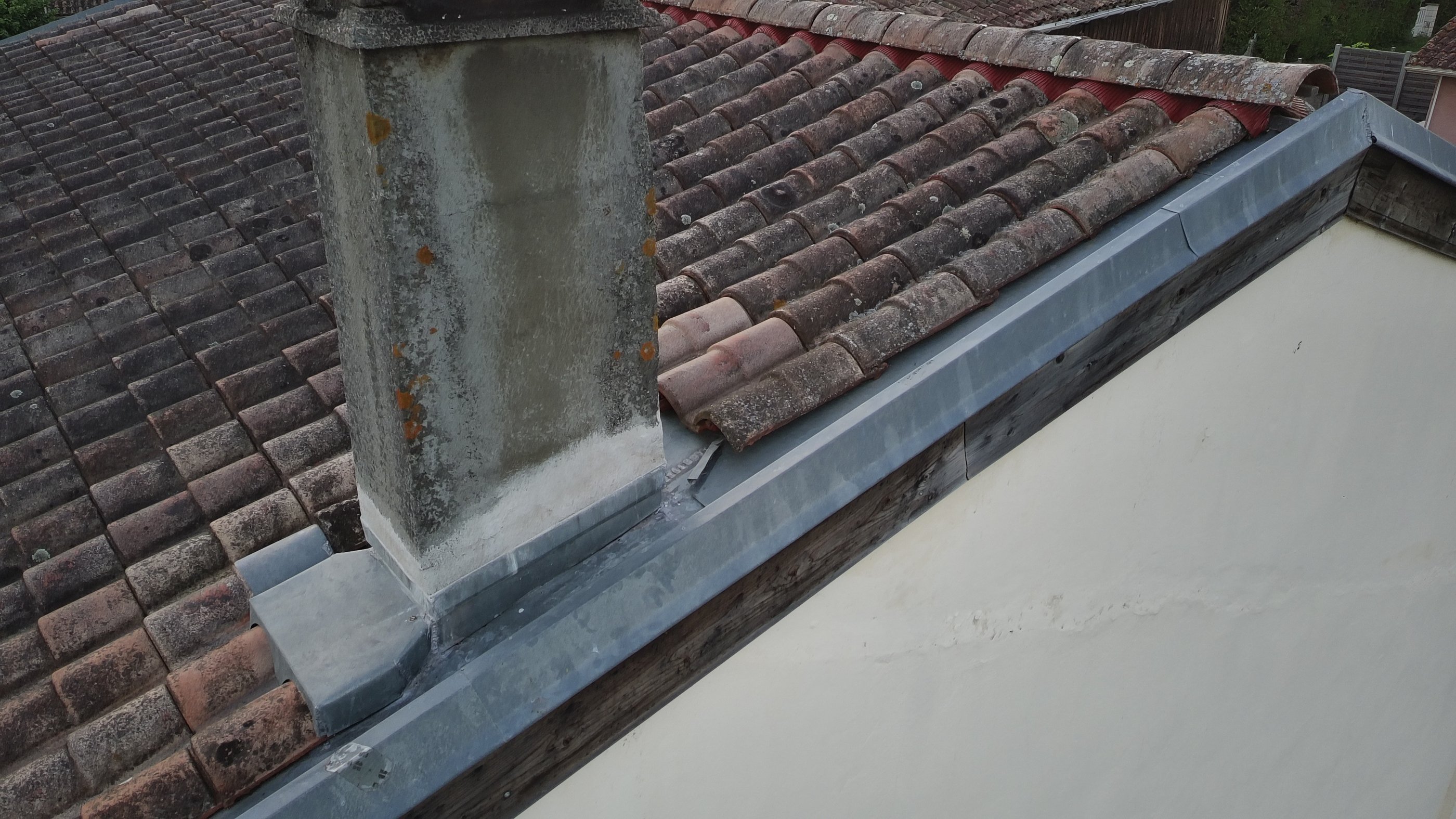 Installation de fléchage et gouttière en zinc sur un toit en tuile avec une cheminée en bêtonen 