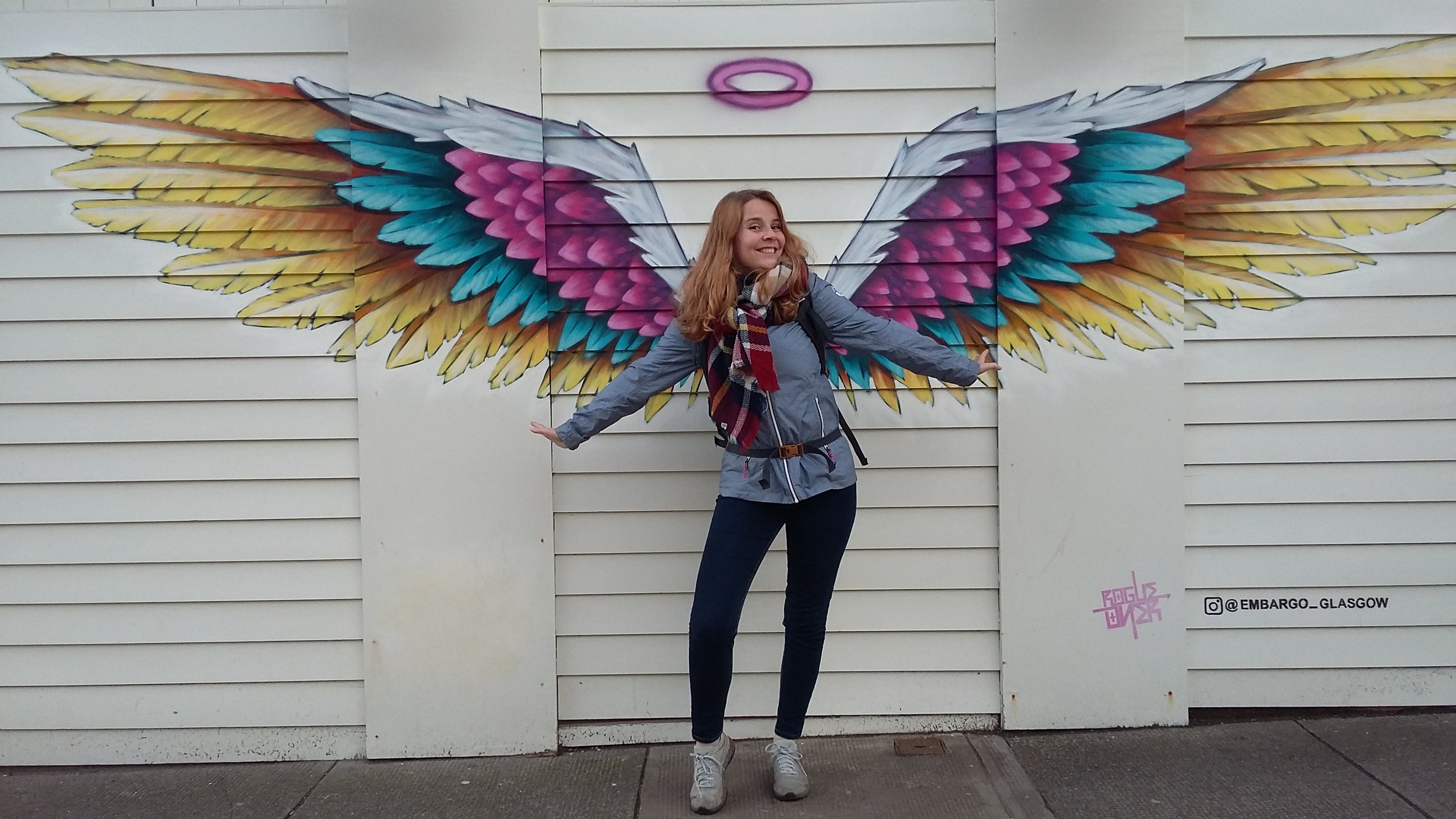 a woman standing in front of a wall with a large colorful angel wings