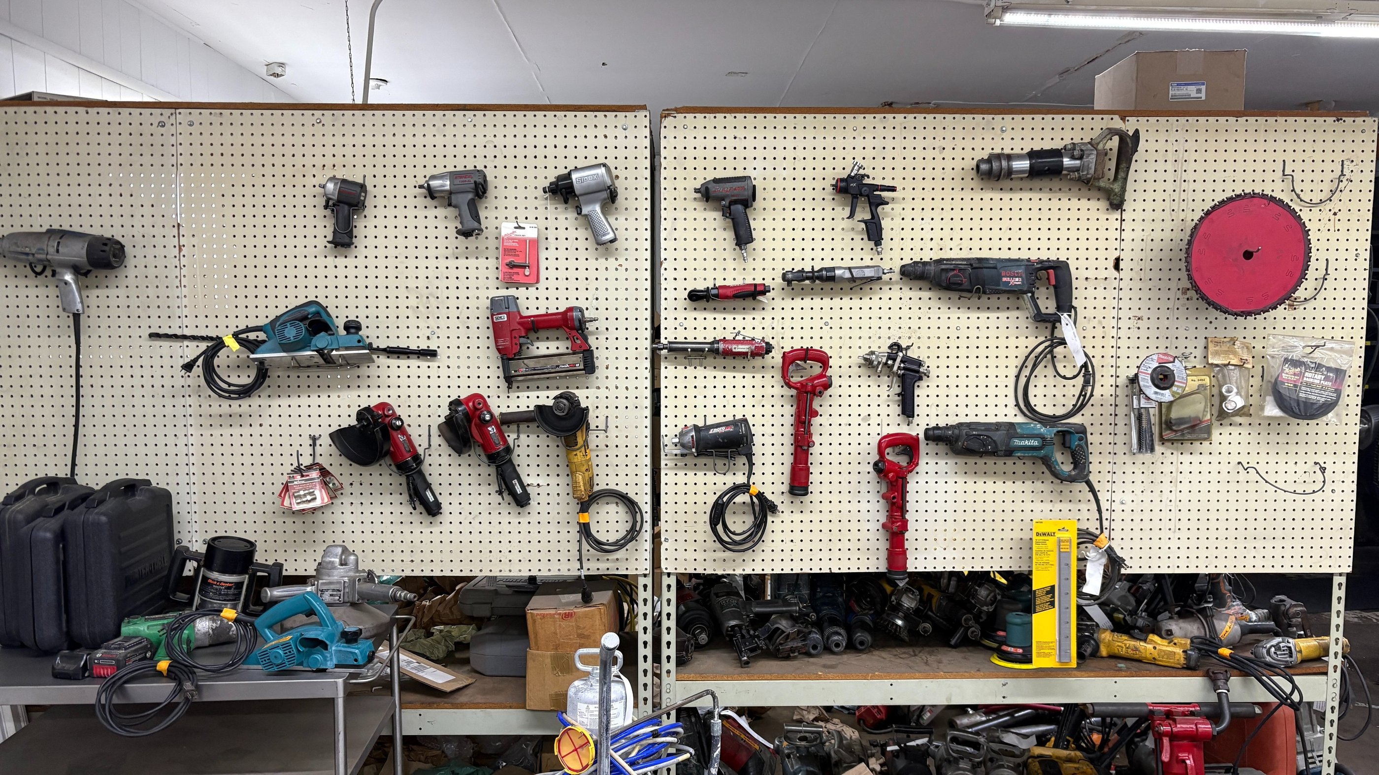A collection of electric power tools and pneumatic equipment hanging on a pegboard workshop wall.