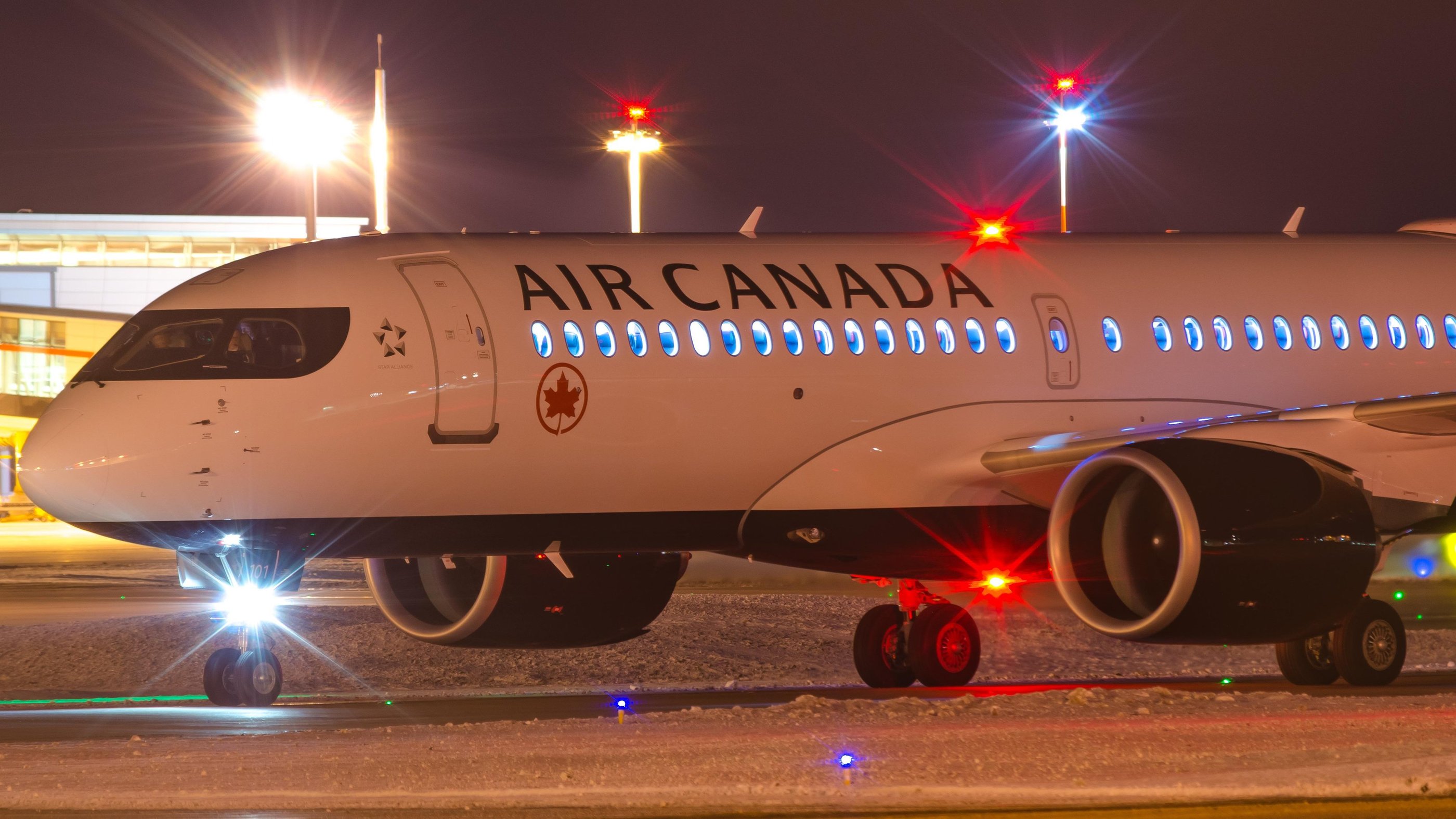 An Air Canada airplane taxis on a snow-covered runway at night with bright terminal lights.VIREMONT 