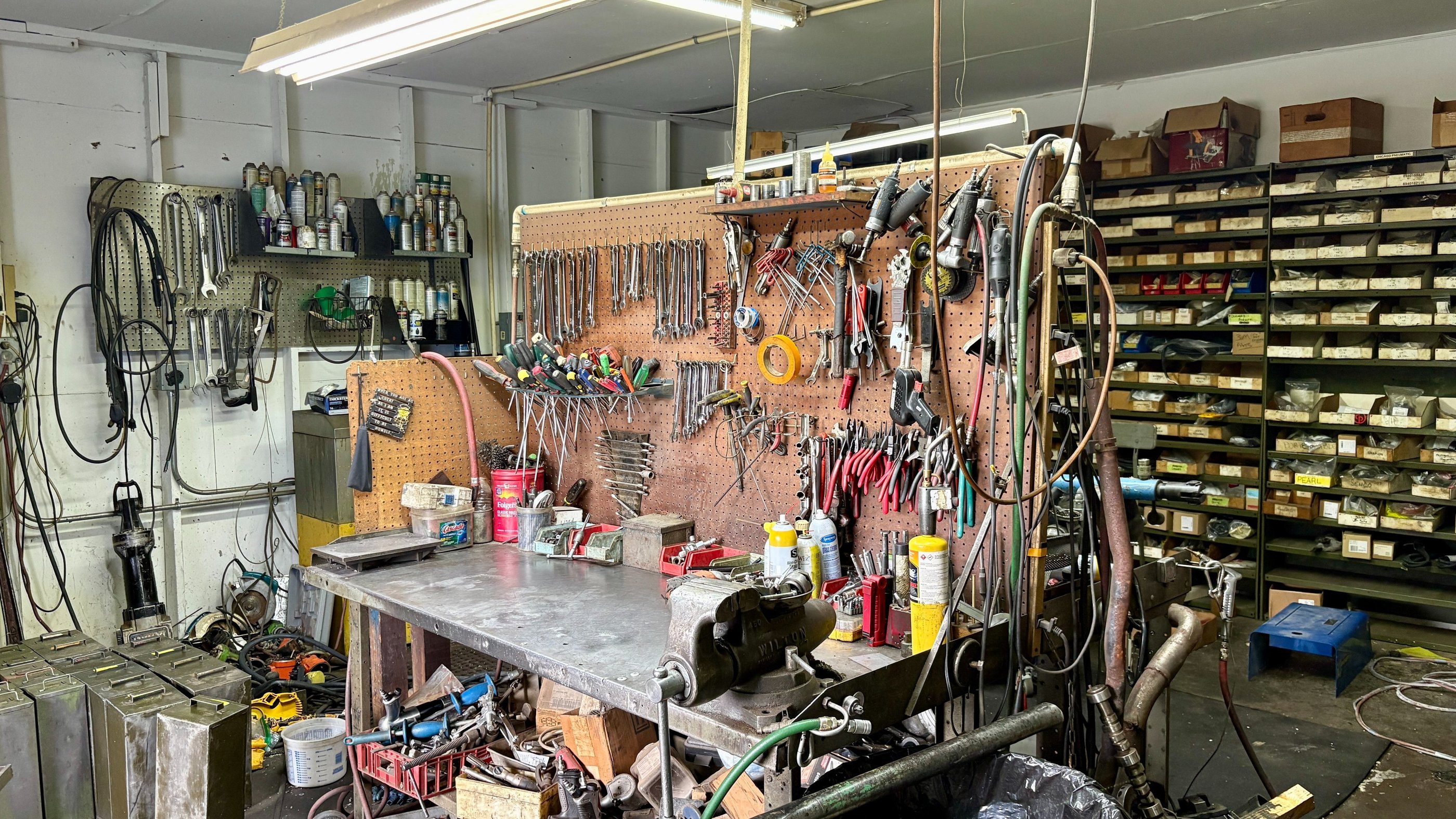 Organized mechanical workshop with hand tools on pegboards above a metal workbench with a vise.